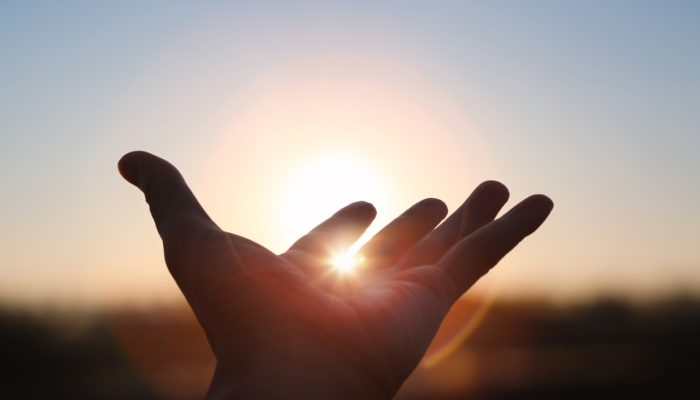Hands stretched out toward the rising sun at New Year's sunrise, brilliant light shining between fingers, future hope and hope concept